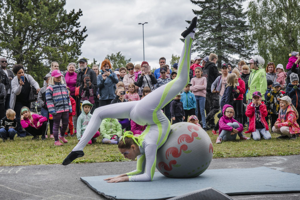 Lastentapahtumassa akrobaatti esiintyy puistossa, taustalla yleisöä.