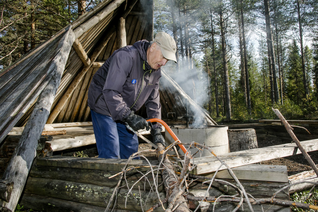 Mies sahaa polttopuuta laavulla.