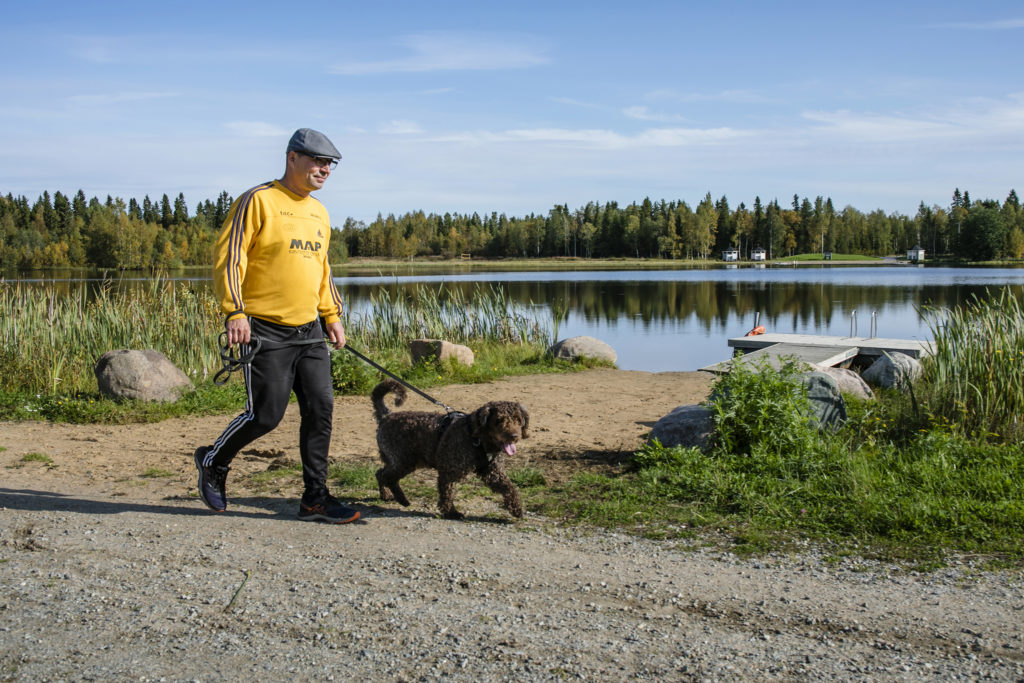 Mies koiran kanssa kävelylenkillä järven rannalla.