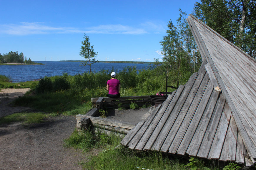 Nainen istuu laavulla merenrannalla.