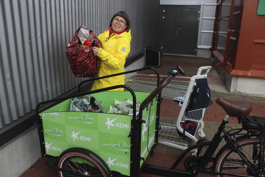 Nainen pakkaa ruokakasseja polkupyörän kuljetuskärryyn.