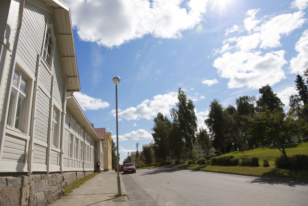 Näkymä kesäiselle kadulle, vasemmalla puurakennus, oikealla puistoa.