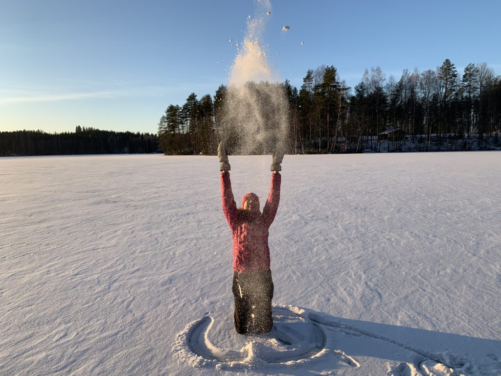 Nainen hangella heittelemässä lunta.