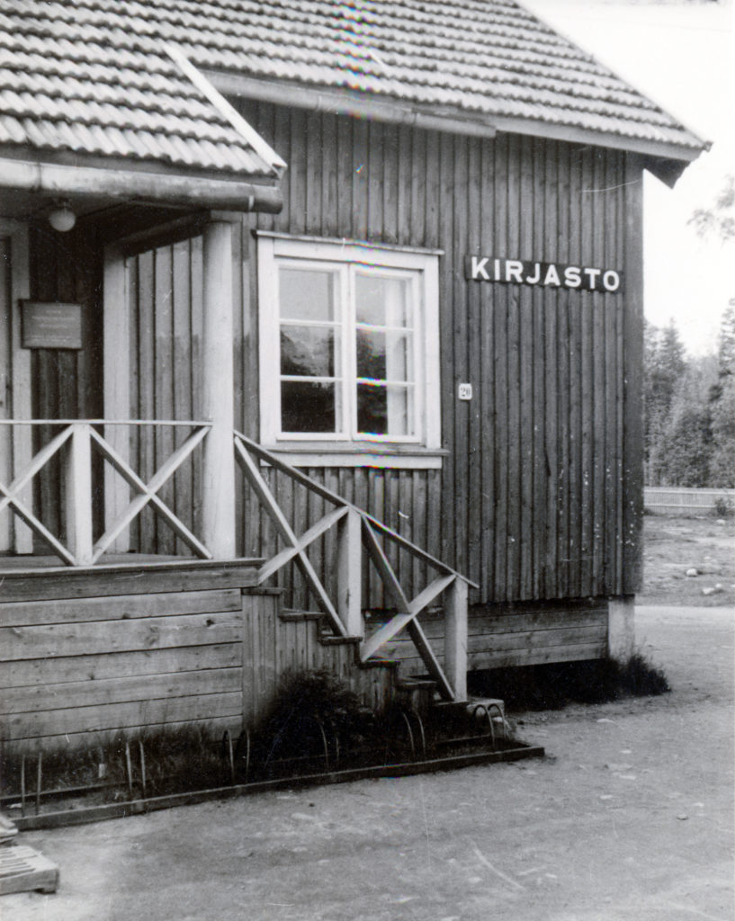 Sivukirjasto vanhassa puurakennuksessa, mustavalkoinen ulkokuva.