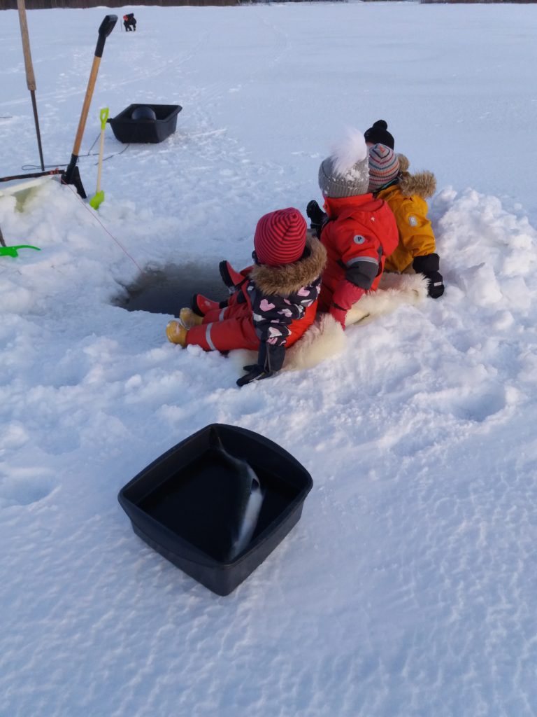 Lapsia istuu avannon vierellä jäällä.