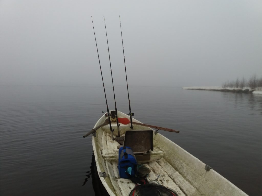 Sumuinen merimaisema. Etualalla vene, jossa kiinnitettynä kalastusvapoja.