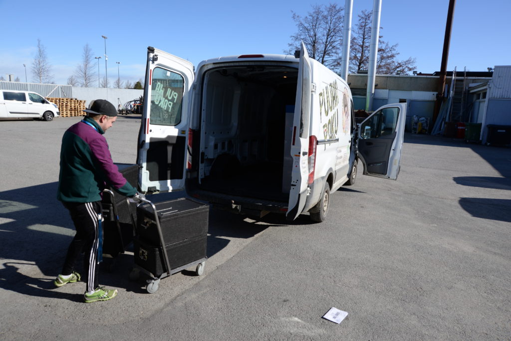 Mies vie kärryillä ruokalaatikoita pakettiautoon.