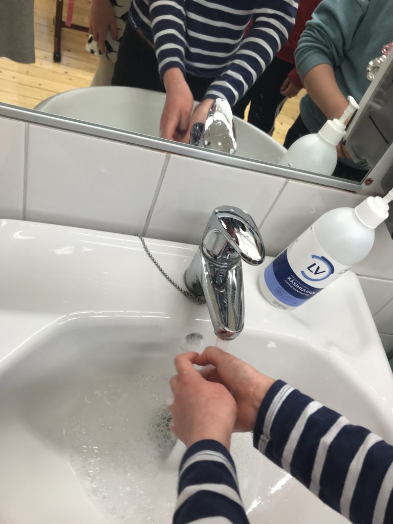 Lapset pesemässä käsiä koulussa lavuaarin luona.