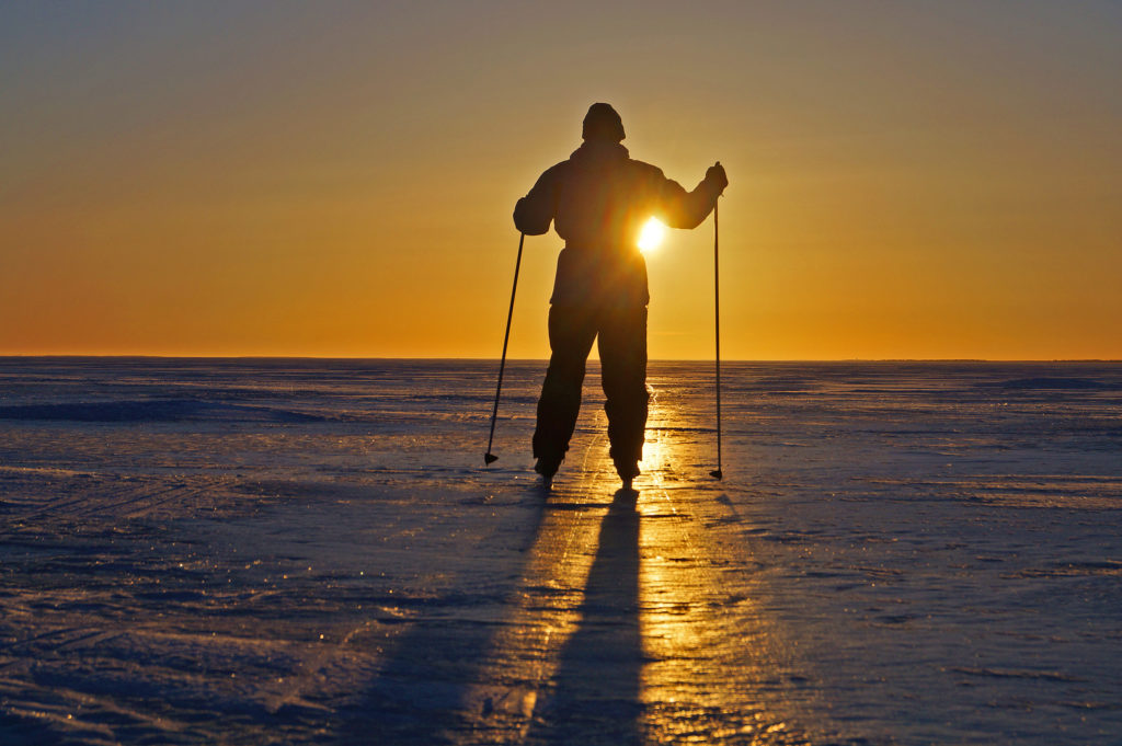 Mies hiihtää jäällä vasten auringonlaskua