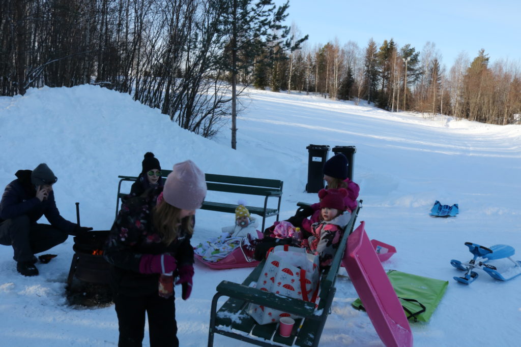 Pulkkamäen juurella perhe nuotiolla eväiden kanssa.