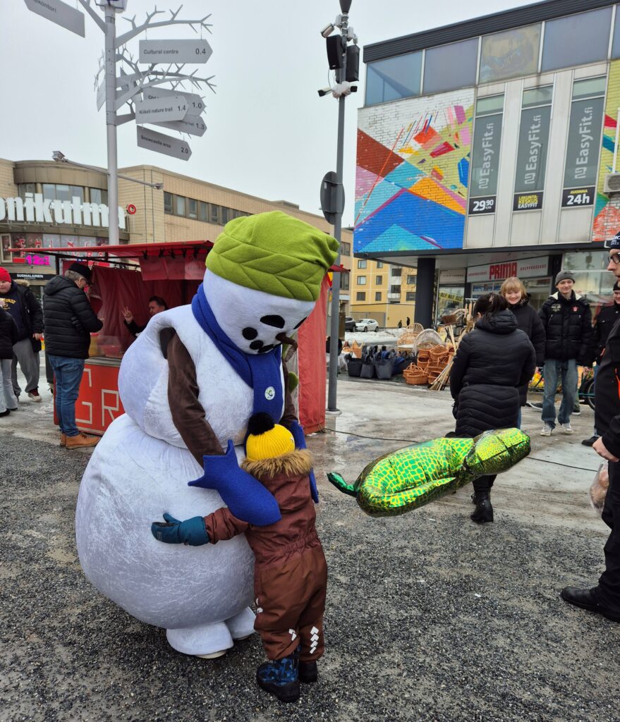 Lumiukkomaskotti ja pikkulapsi halaavat ulkokuvassa.