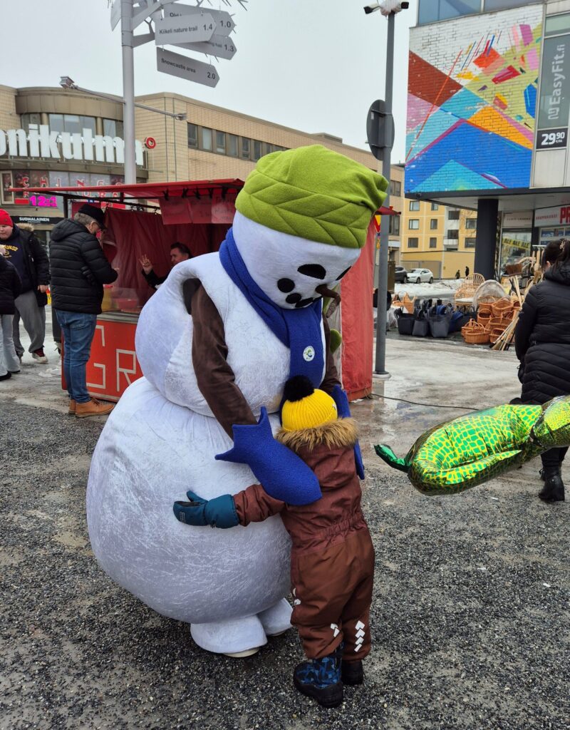 Lumiukkomaskotti ja pikkulapsi halaavat ulkokuvassa.