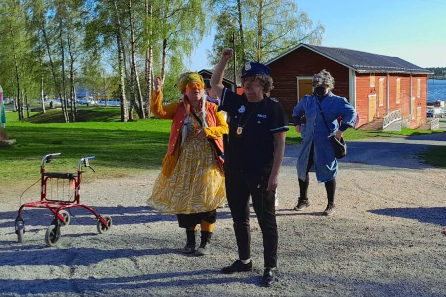 Teatteriasuihin pukeutuneita ihmisiä pihalla auringonpaisteessa.