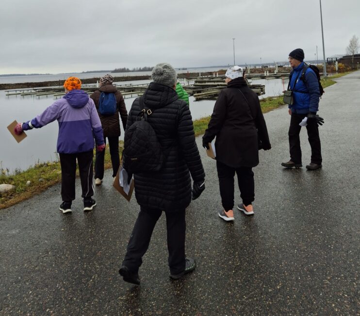 Ihmisiä syyssäässä ulkona meren rannalla.