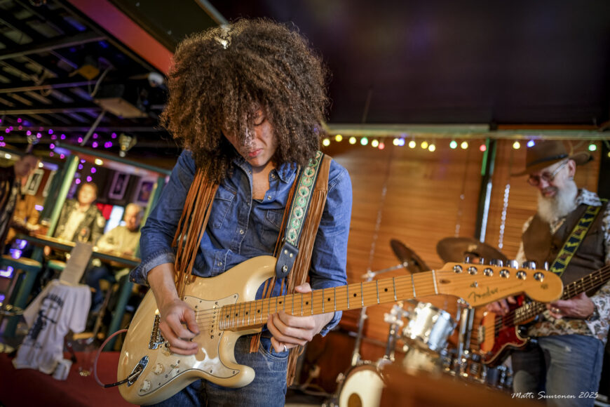 Afrotukkainen soittaja näppäilee sähkökitaraa keskittyneesti kumarassa.