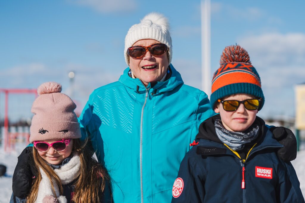 Vanhempi nainen aurinkoisessa talvimaisemassa kaksi lasta kainalossaan.