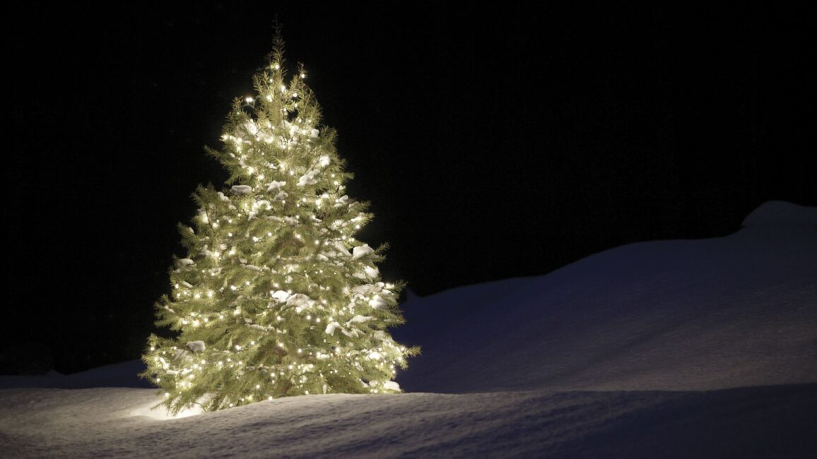Valaistu joulukuusi lumisessa maisemassa.